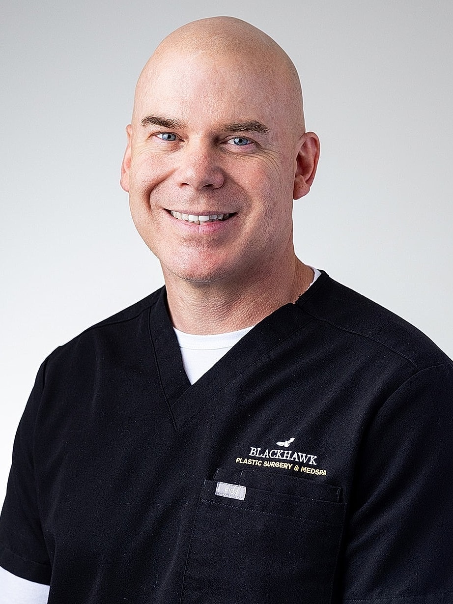 Smiling doctor in black scrubs with logo.