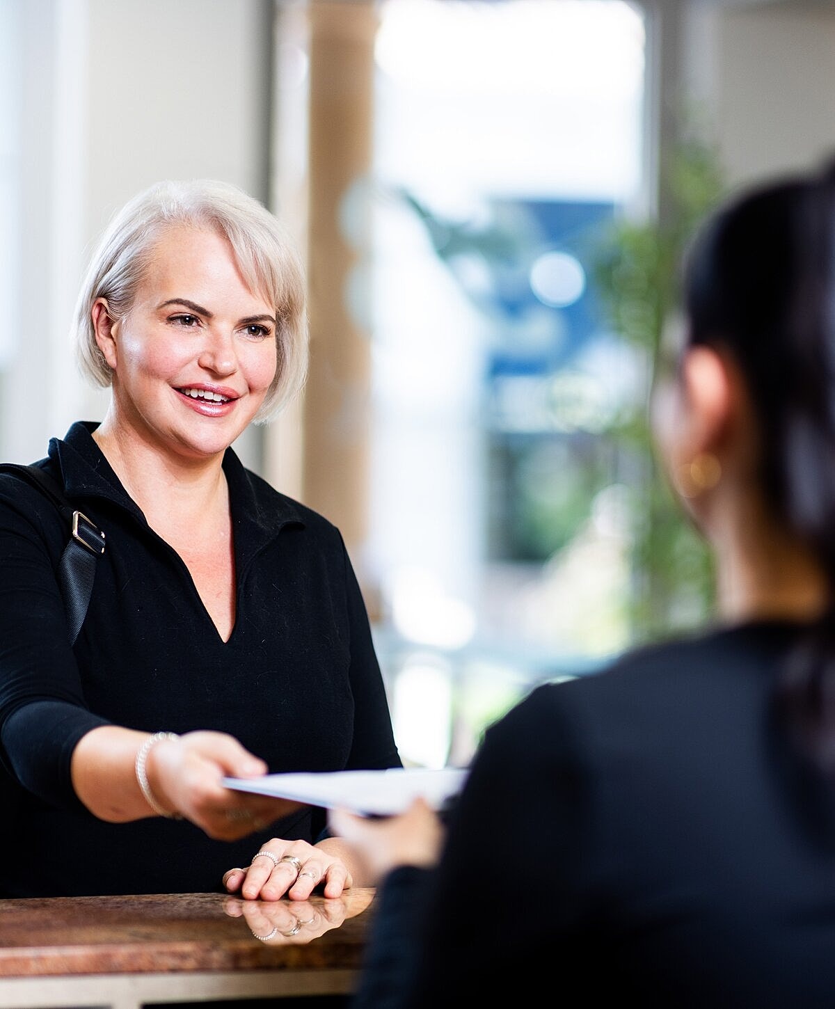Woman handing documents to receptionist at desk.