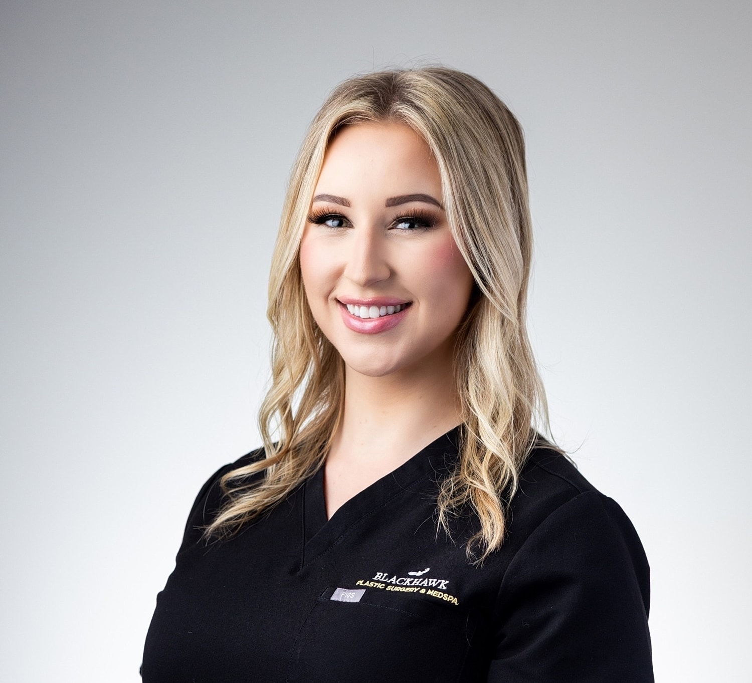 Smiling professional in medical attire against neutral background.