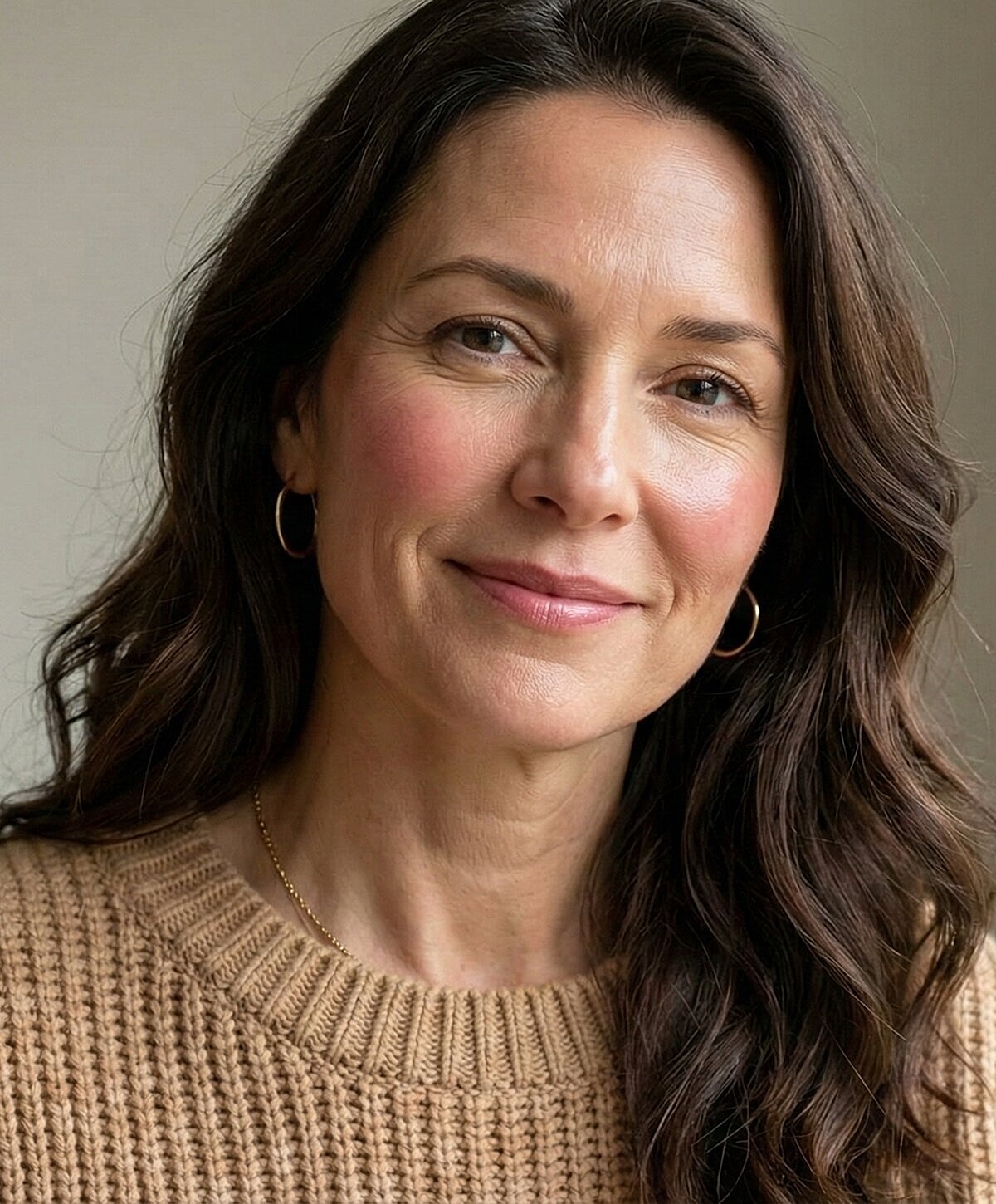 Smiling woman with long, wavy hair in sweater.