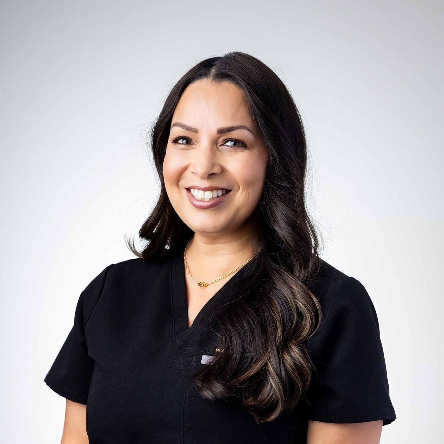 Smiling professional in medical attire against backdrop.