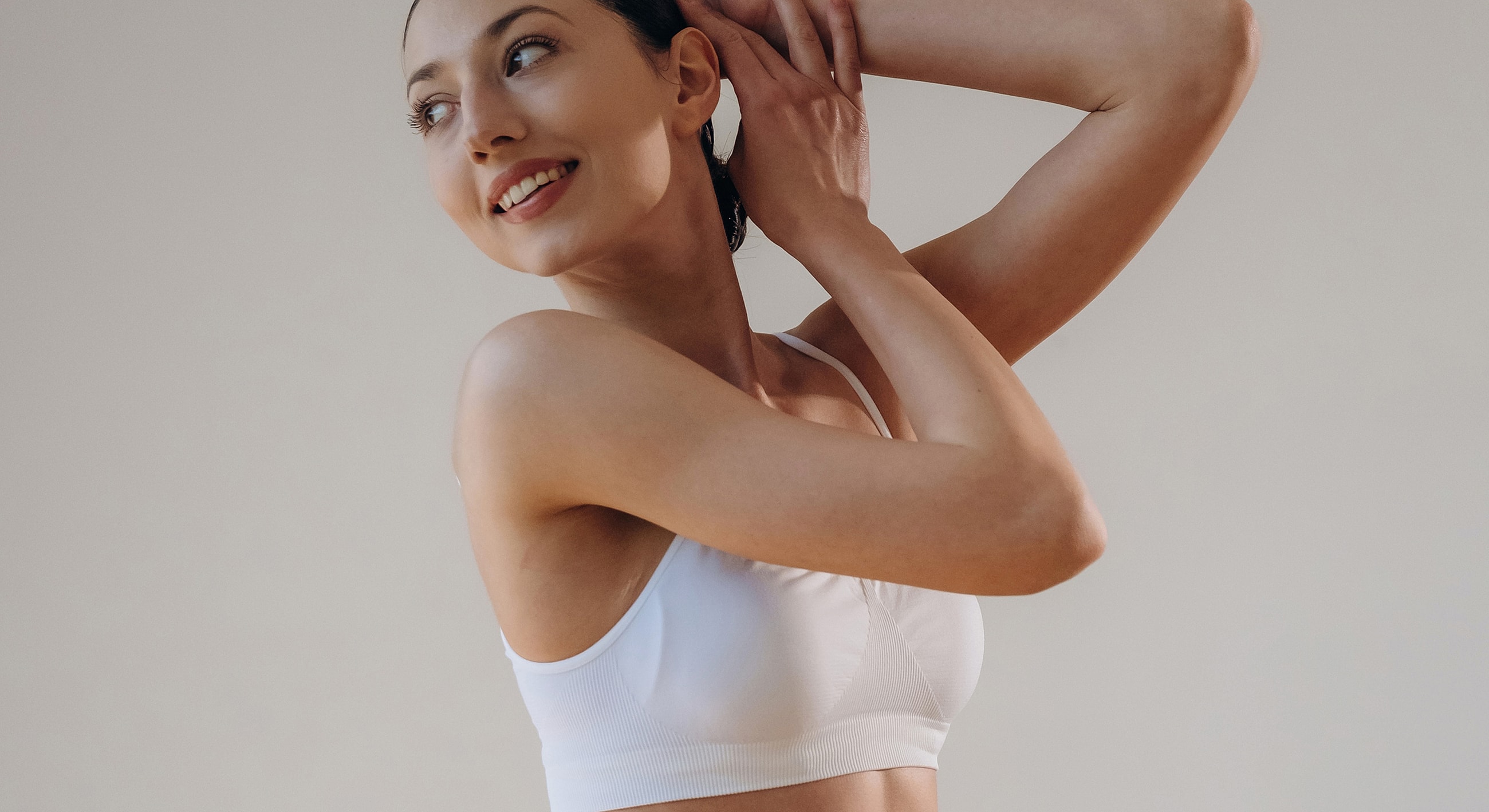 Woman styling hair in a white sports bra.