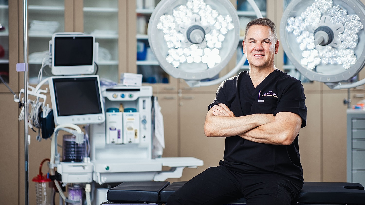 Smiling doctor in surgical environment, arms crossed.